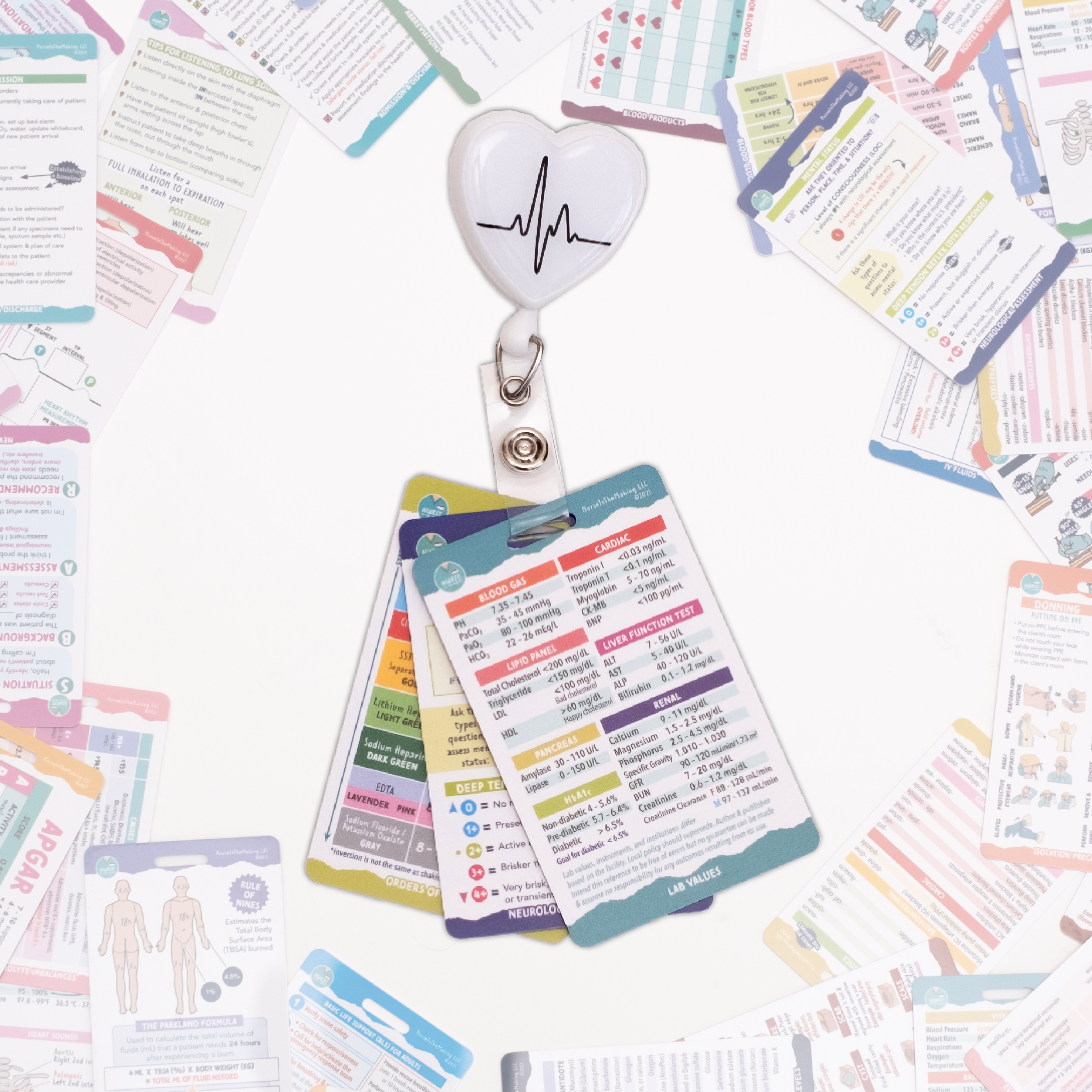 A set of nursing badge cards attached to a retractable badge reel with a heart and ECG line design. The cards display colorful medical reference information. Additional badge cards and study materials are scattered in the background.