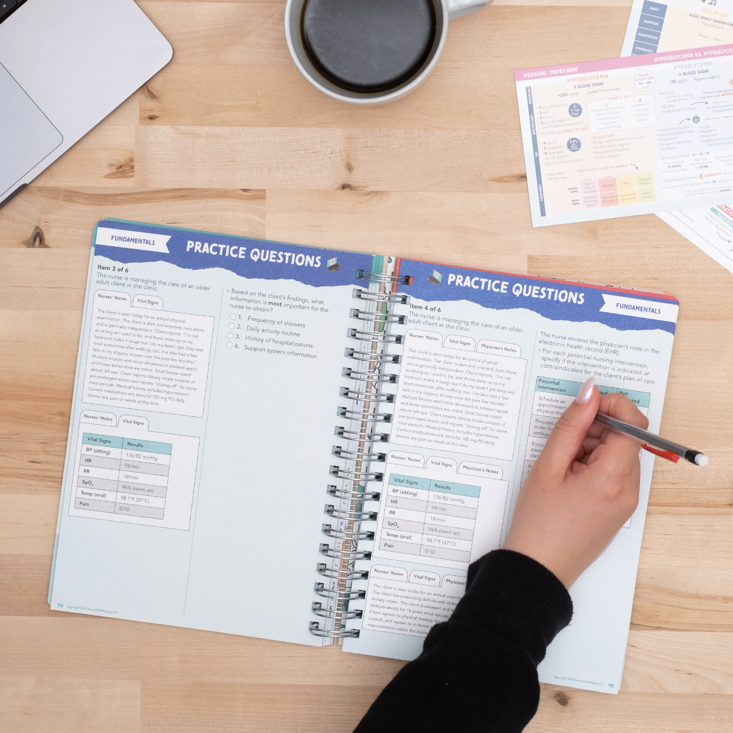 A student writing in an open NCLEX Study Notebook, completing practice questions. The pages contain structured question prompts, answer spaces, and explanations. A laptop, coffee cup, and additional study materials are on the wooden desk, setting a focused study atmosphere.