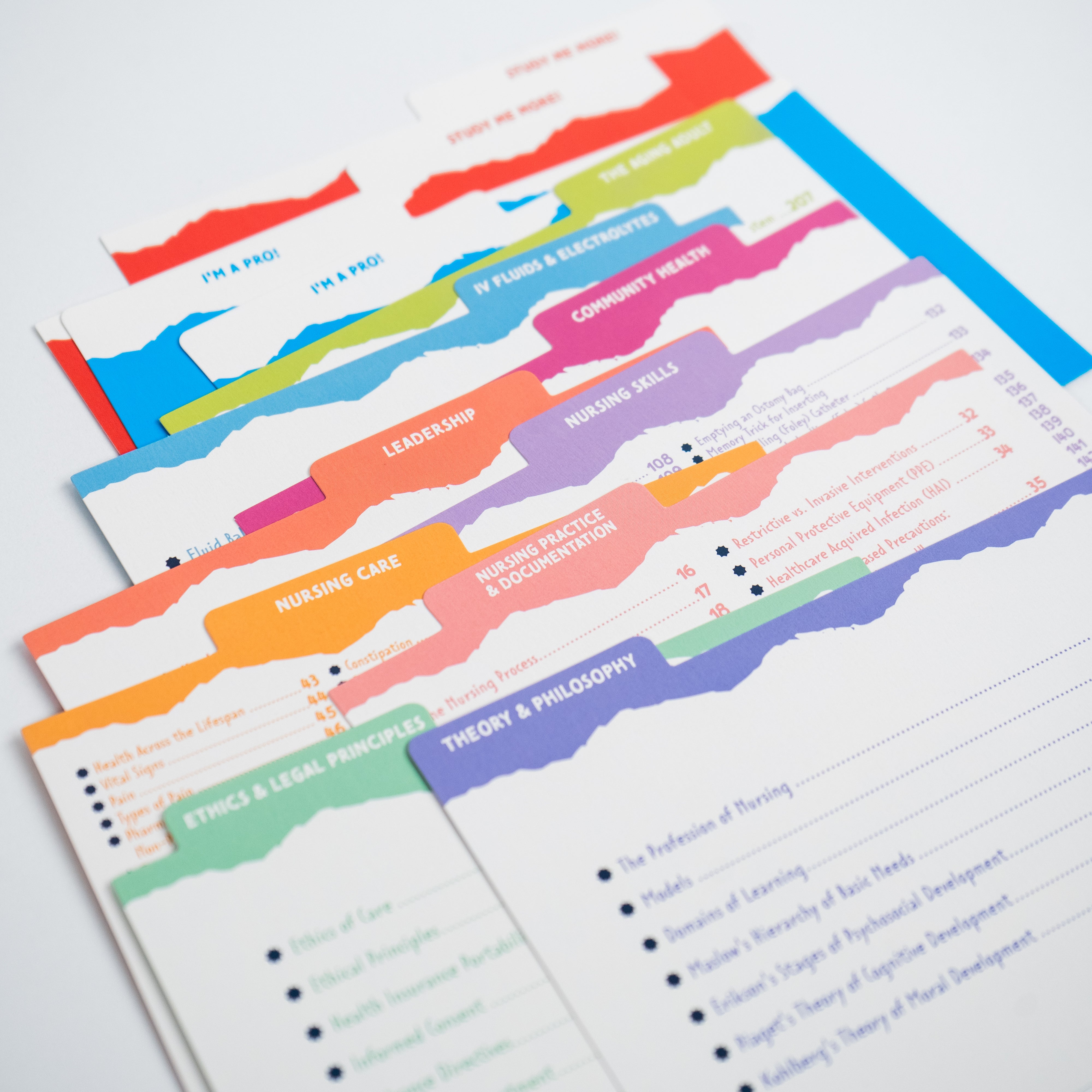 A close-up of colorful fundamentals flashcard dividers, each labeled with different nursing topics. The dividers have jagged edges and bright colors, including red, blue, green, orange, and purple. Topics such as “Leadership,” “Nursing Skills,” “Ethics & Legal Principles,” and “Theory & Philosophy” are visible. The background is white, with the dividers layered on top of each other.