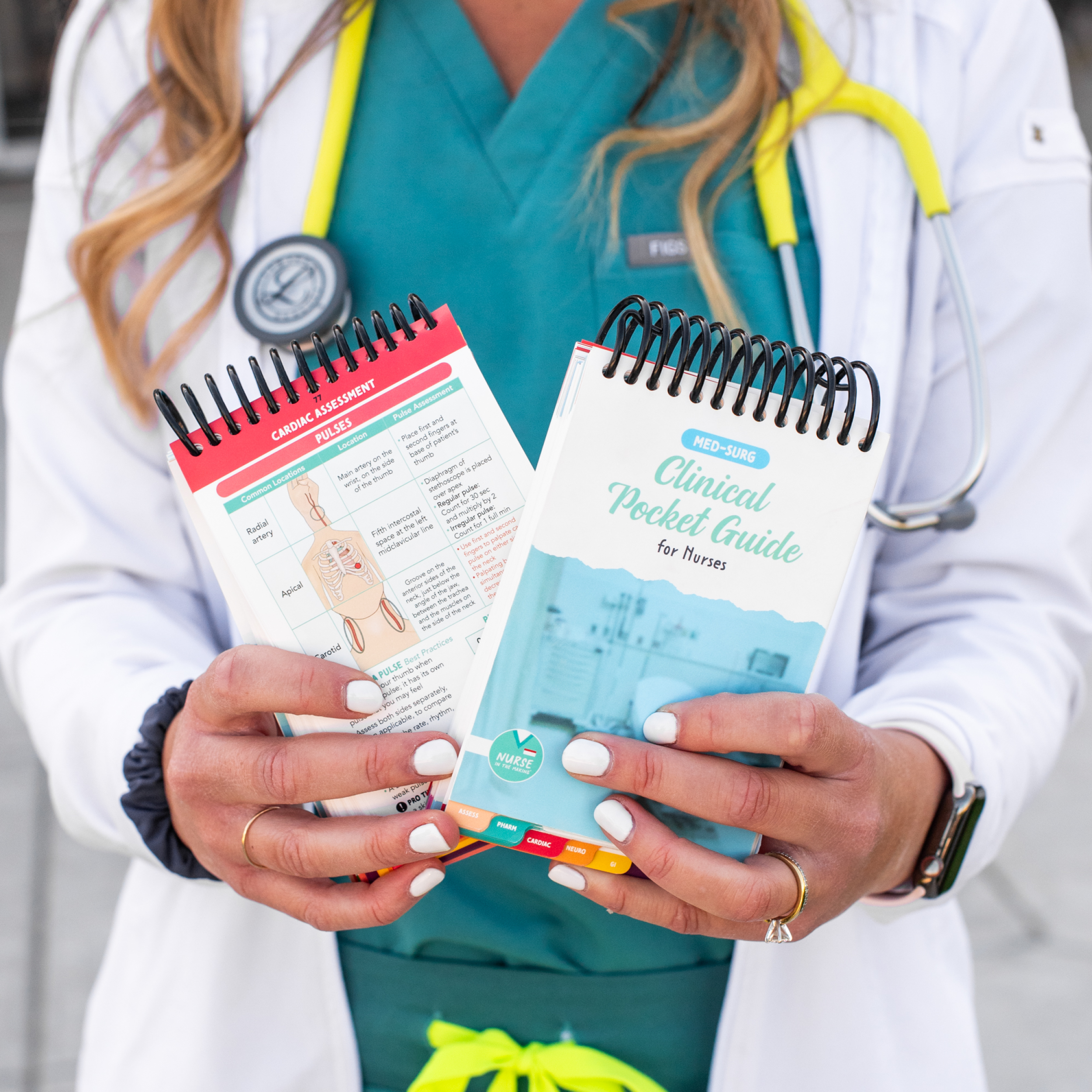 A nurse in green scrubs and a white lab coat holds two Clinical Pocket Guides for Nurses. One guide has a blue-toned cover featuring a hospital scene, while the other is open, displaying a colorful medical illustration and quick-reference notes. The guides are compact, spiral-bound, and feature color-coded tabs for easy navigation. The nurse’s stethoscope hangs around her neck, and she has neatly manicured nails with white polish.