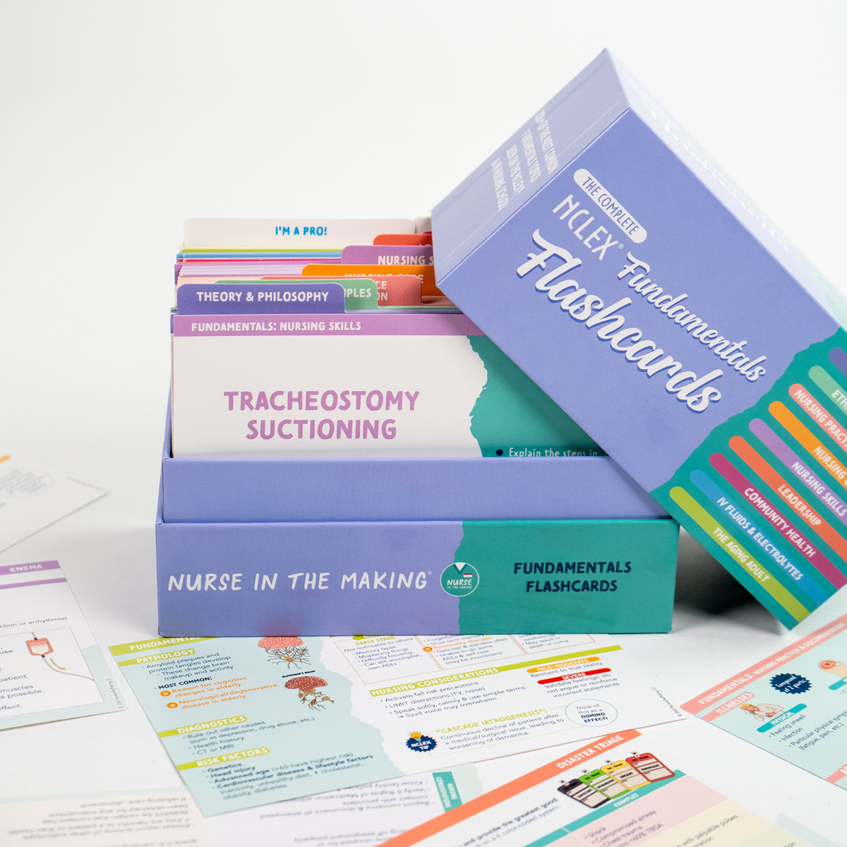 Open box of NCLEX Fundamentals Flashcards from Nurse In The Making, showcasing organized flashcards on essential nursing topics like Tracheostomy Suctioning, Theory & Philosophy, and Nursing Skills. Additional colorful flashcards with medical illustrations are spread around the box.