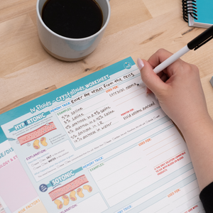 A nursing student fills out a laminated IV fluids study template using a dry-erase marker. The worksheet is structured with colorful sections detailing hypertonic and isotonic solutions, their effects, and clinical applications. A cup of coffee and a notebook are nearby, suggesting a study session. The reusable design allows for practice and review.