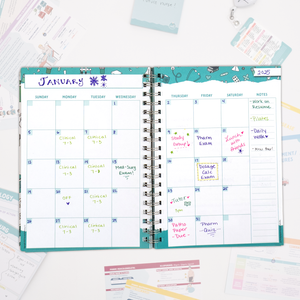 An open spiral-bound planner displays a monthly calendar view for January. The pages are filled with handwritten notes in different colors marking study sessions, exams, and clinical rotations. Various study materials and flashcards surround the planner on a white surface.