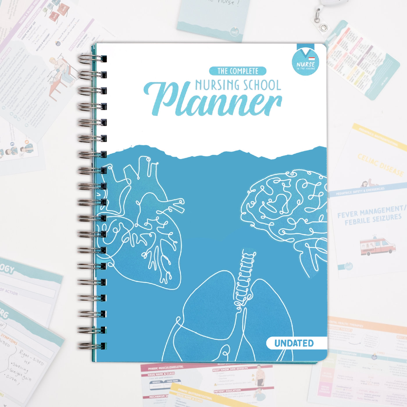 Nurse In The Making's Nursing School Planner with a blue and white cover featuring anatomical illustrations of the heart, lungs, and brain. The title “The Complete Nursing School Planner” is prominently displayed in bold lettering, with “Undated” noted in the bottom right corner. The planner is spiral-bound and laid flat on a white background, surrounded by various nursing study materials and flashcards. The cover design is clean and professional, with a medical-themed aesthetic.